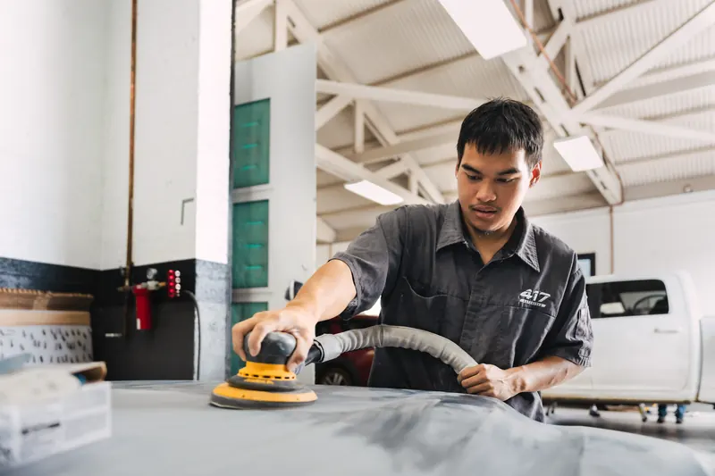 A technician sanding a body panel smooth before refinishing